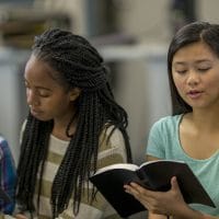 | A multi-ethnic group of high school age students are sitting together reading the Bible together during a Bible study.