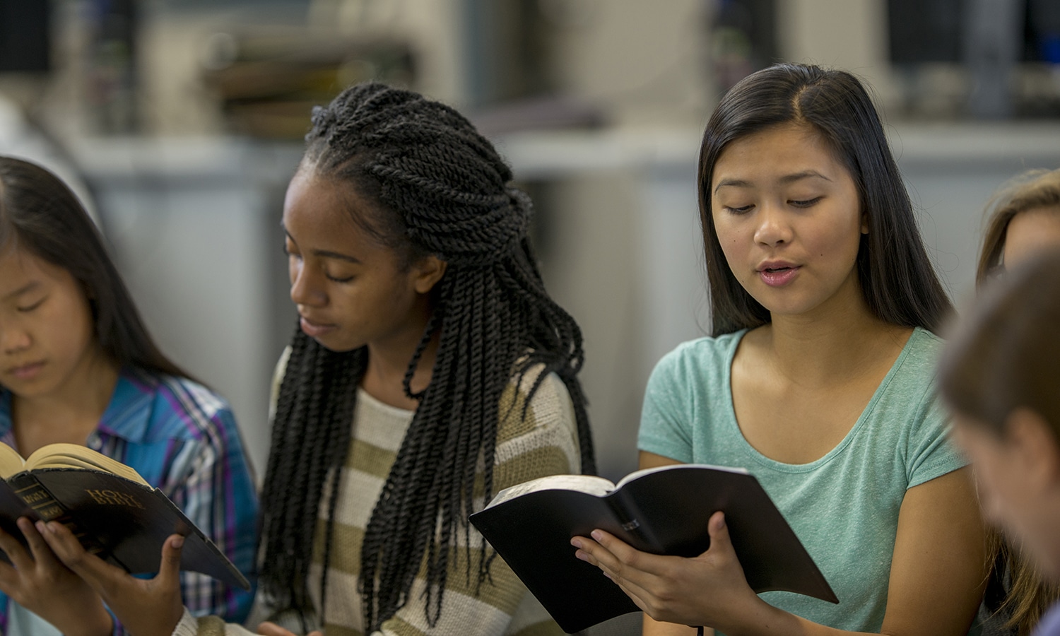| A multi-ethnic group of high school age students are sitting together reading the Bible together during a Bible study.