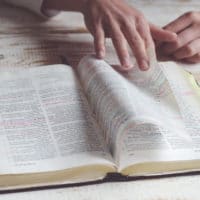How To Memorize Scripture | The Navigators Bible Study Resources | hands paging through a bible on a wood desk