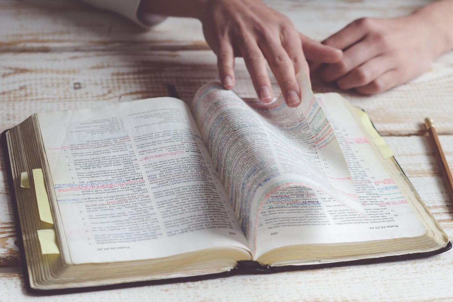 How To Memorize Scripture | The Navigators Bible Study Resources | hands paging through a bible on a wood desk