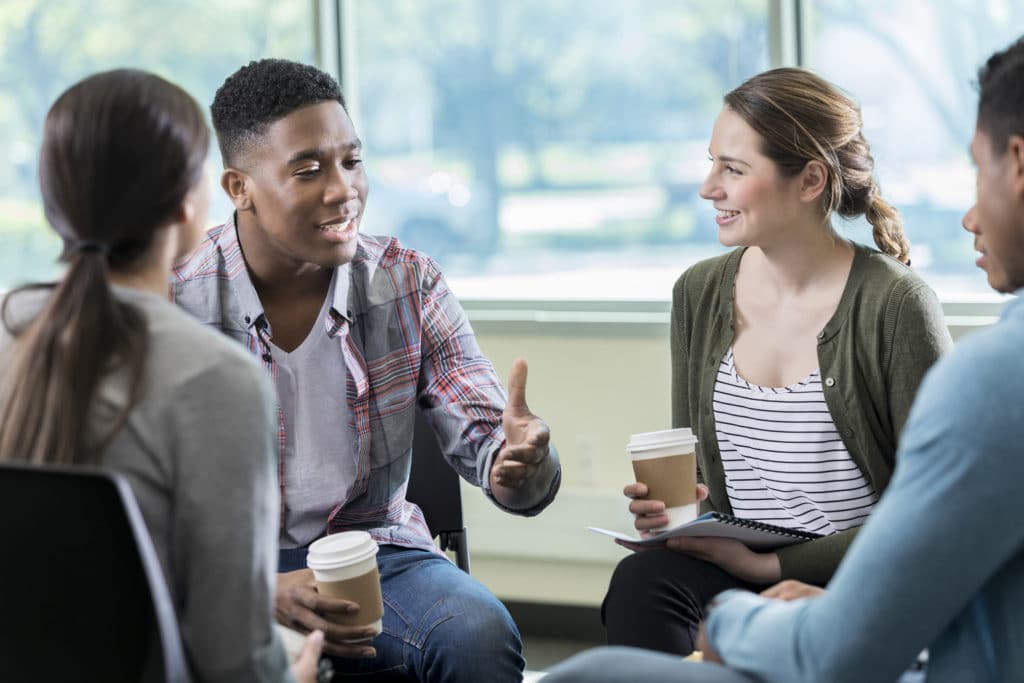 Building Relationships in a Small Group | Storytelling | The Navigators | Young African American man gestures while discussing something with a group of friends. They are listening intently to him as he talks.