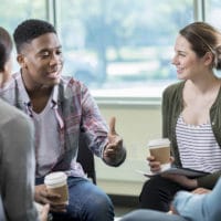 Building Relationships in a Small Group | Storytelling | The Navigators | Young African American man gestures while discussing something with a group of friends. They are listening intently to him as he talks.