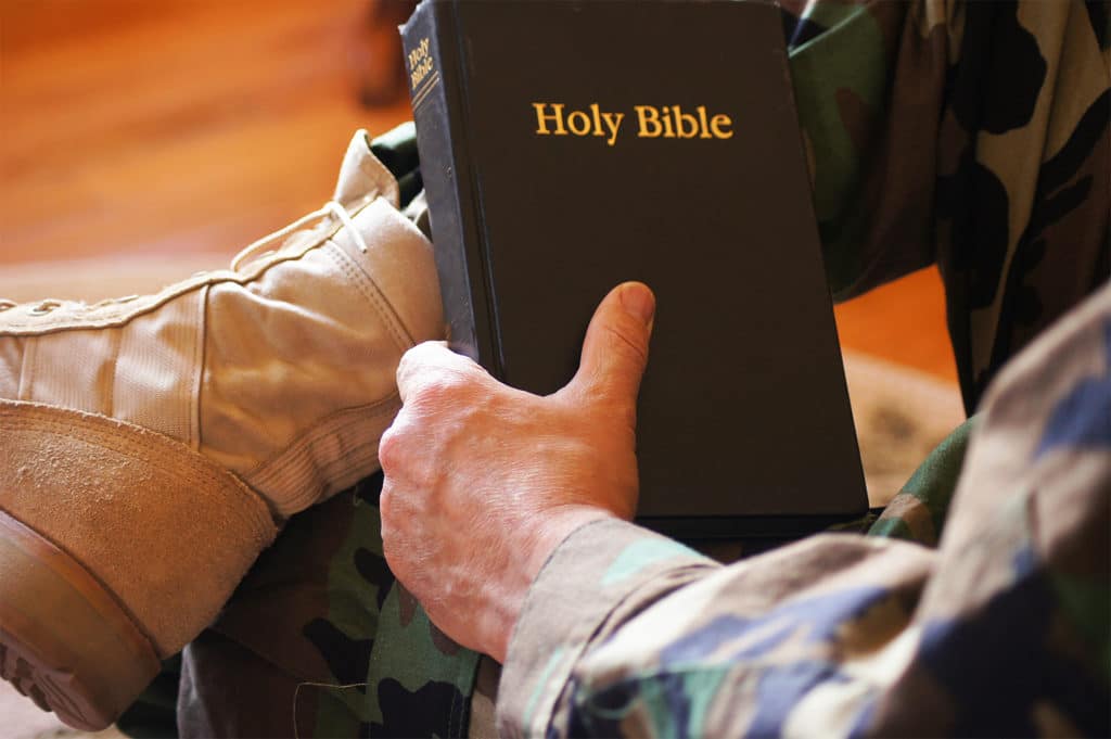 Soldier wearing camouflage clothes and military boots holding a Bible