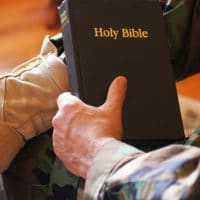 Soldier wearing camouflage clothes and military boots holding a Bible