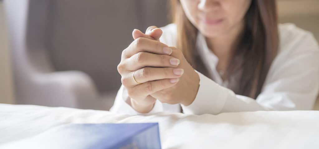 Prayers Across Miles | The Navigators International Student Ministry | Woman in her room holding her hands together on her Bible