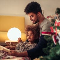 Keeping Christ as the Focus of Christmas | Navigators Bible Study Resource | Dad reading fairy tales to his daughter while lying next to Christmas tree