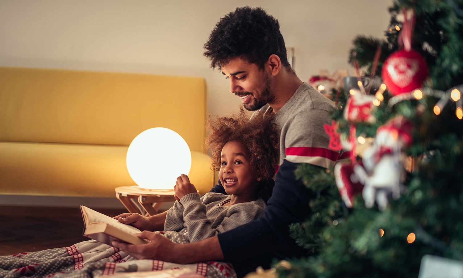 Keeping Christ as the Focus of Christmas | Navigators Bible Study Resource | Dad reading fairy tales to his daughter while lying next to Christmas tree