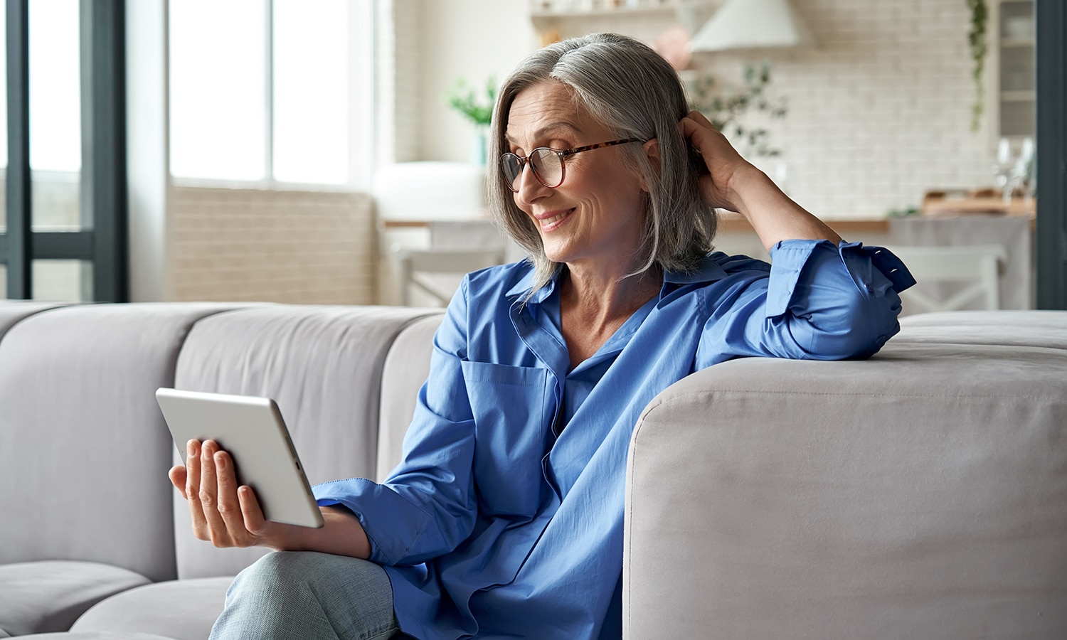 Women’s Bible Study: Living for What Really Matters | Navigators Bible Study Resource | Happy 60s older mature middle aged adult woman holding digital tablet computer conference calling by social distance virtual family online chat meeting or watching video sitting on couch at home.