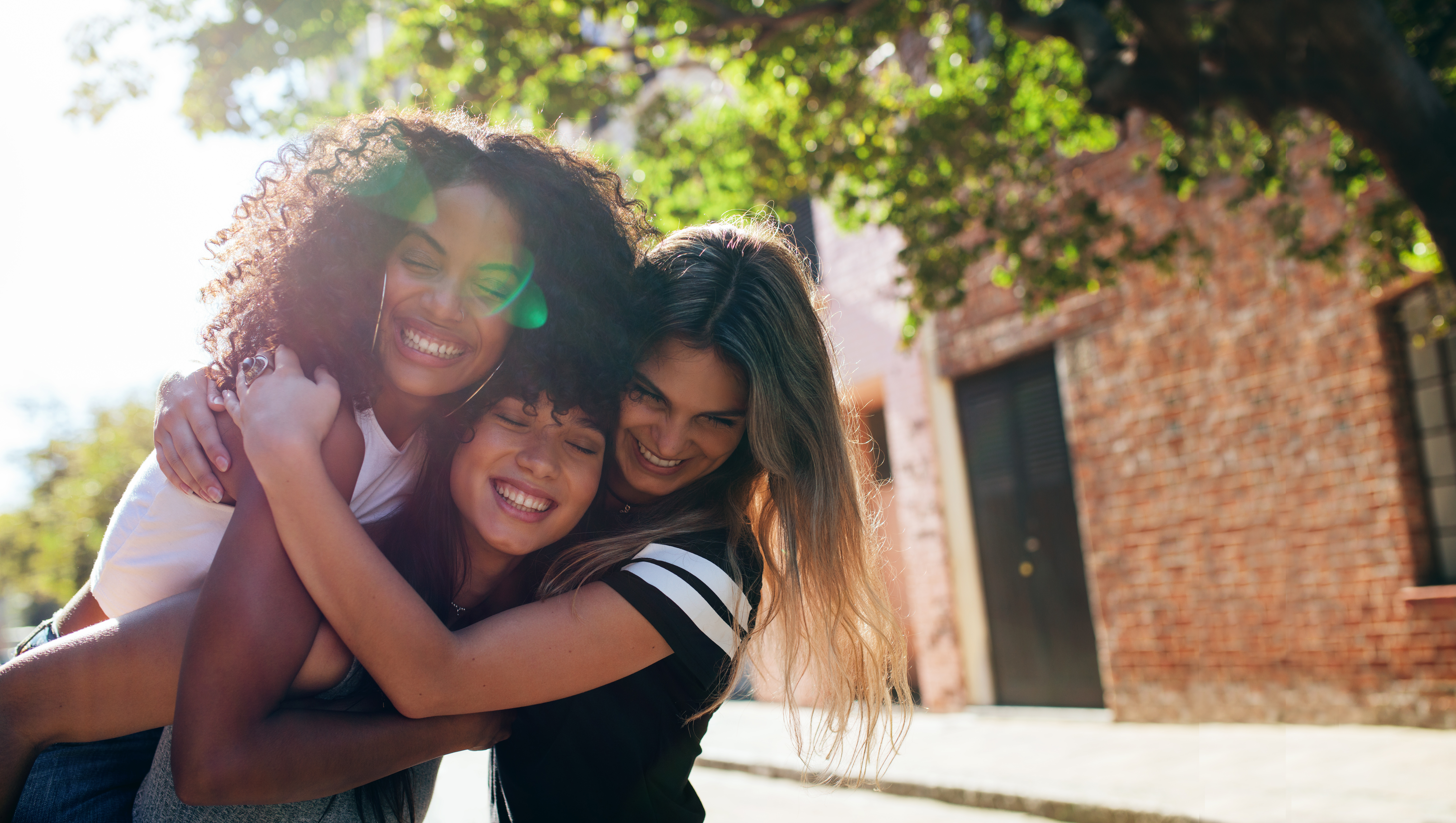 Three happy young women embracing each other – intentionally encouraging each other in discipleship through a Navigators Digital Discipleship Journey.
