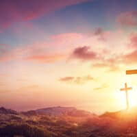 Three crosses on a hill with the sun shining through the clouds