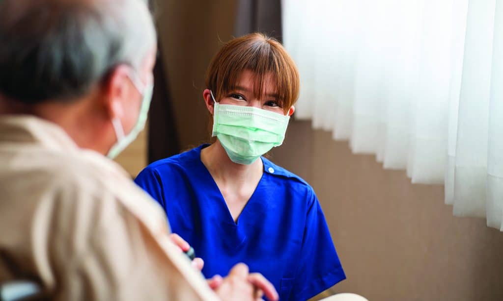 Lifelong Disciplemaker | Navigators Encore | young Asian female nurse kneeling beside senior patient in wheelchair talking, smiling and cheering up in comfort at hospital.