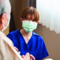 Lifelong Disciplemaker | Navigators Encore | young Asian female nurse kneeling beside senior patient in wheelchair talking, smiling and cheering up in comfort at hospital.