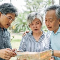 Three elderly Asian people reading the Bible together in the park.