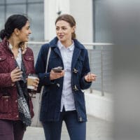 Two women are walking on a city sidewalk talking about how investing in disciples in important.