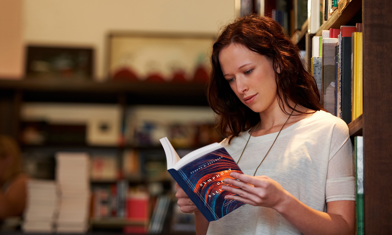 Symphony of Salvation: A 60-Day Devotional Journey through the Books of the Bible | Navigators Bible Study Resource | A young woman lost in the pages of a novel against a backdrop of full bookshelves