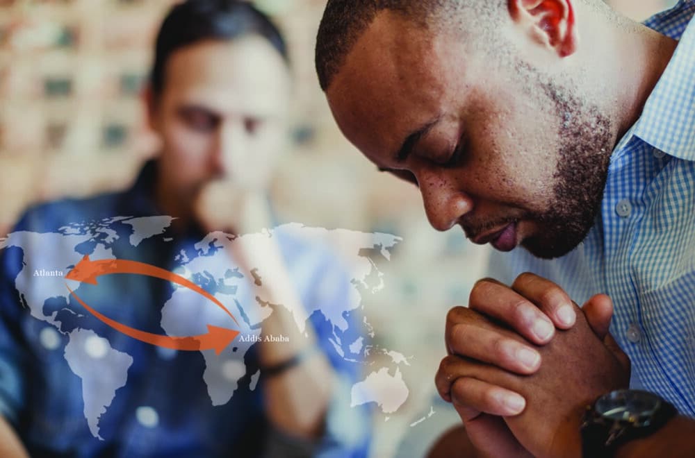 Two men praying over diverse discipleship with a faded world map overlayed on the screen.