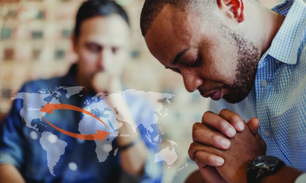 Two men praying over diverse discipleship with a faded world map overlayed on the screen.