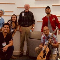 Doctors and nurses standing together, one with a guitar, inside of a hospital foyer.