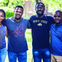 Four young adults at Bowie State University posing for a picture in a park, surrounded by trees.