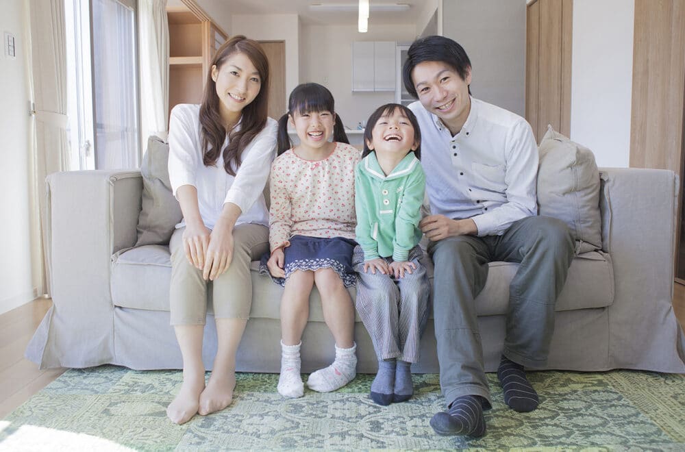 A Japanese husband and wife sitting on their couch with their two children.