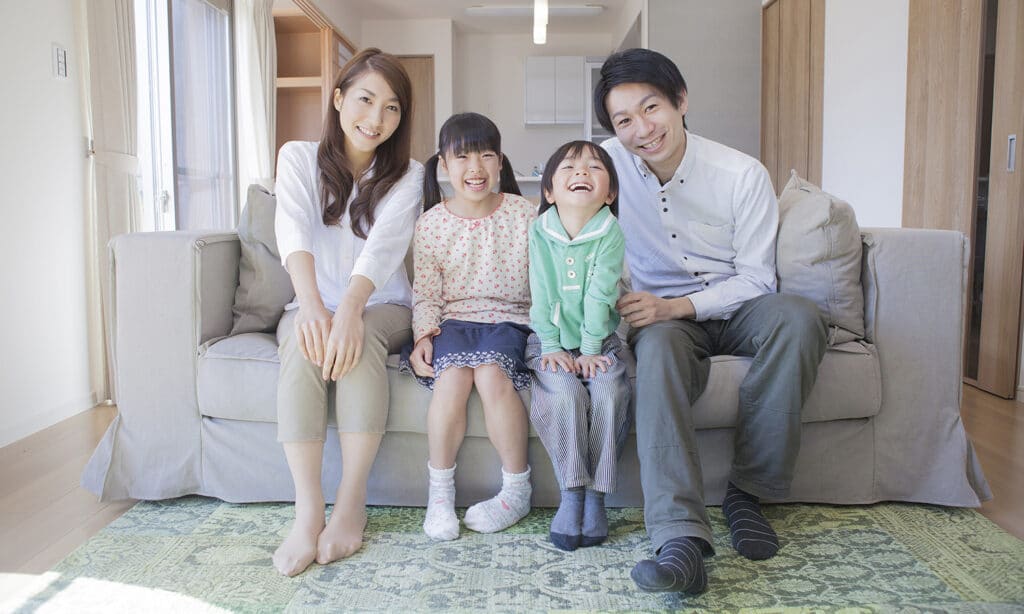 A Japanese husband and wife sitting on their couch with their two children.