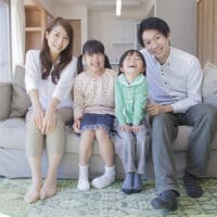 A Japanese husband and wife sitting on their couch with their two children.