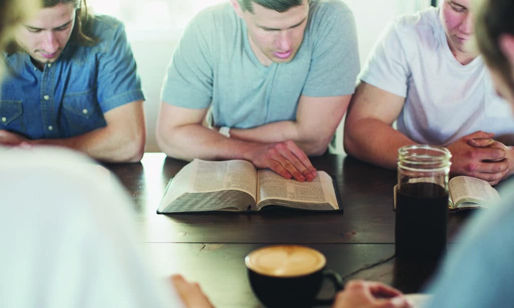 College friends reading The Bible together on a picnic table.