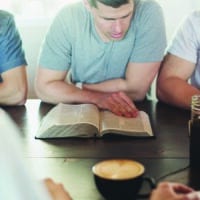 College friends reading The Bible together on a picnic table.