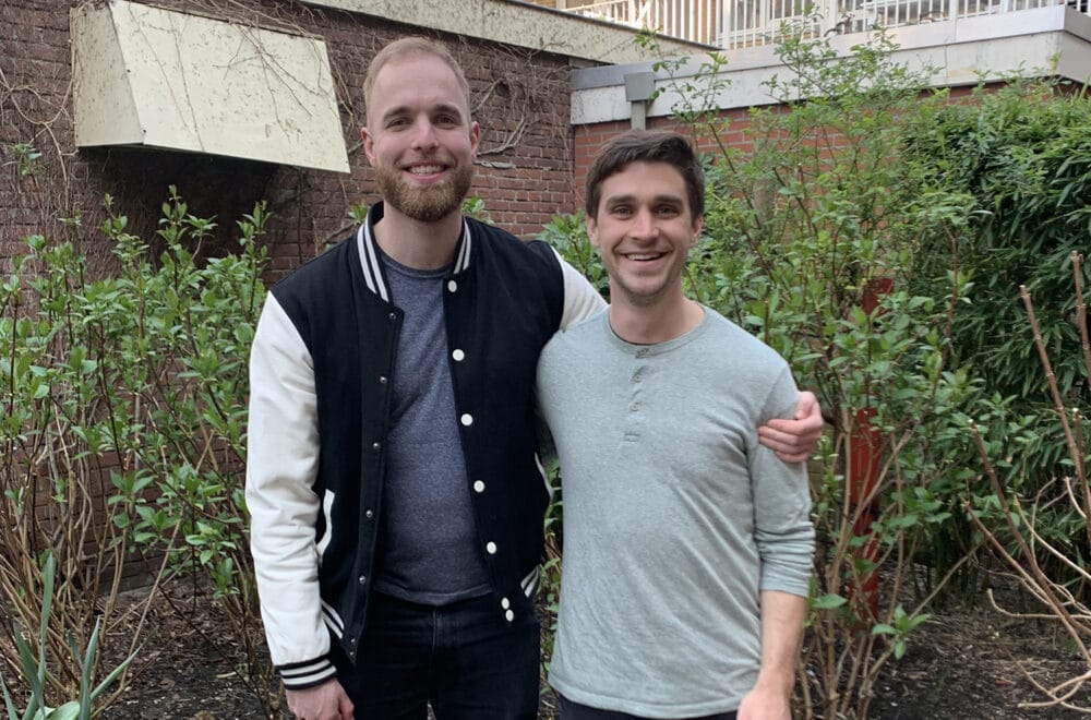 Every and Scott post for a picture in front of a building with shrubs.
