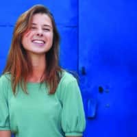 A young woman smiling at the camera with a blue background.