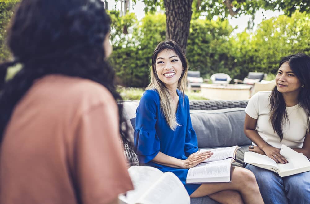Alice Matagora, an author of How to Save The World, talking with two other disciplemakers about discipleship while sitting on outdoor patio furniture.