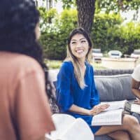 Alice Matagora, an author of How to Save The World, talking with two other disciplemakers about discipleship while sitting on outdoor patio furniture.