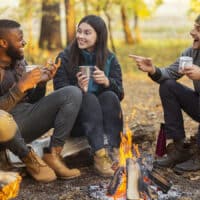 Three young adults sitting around a campfire drinking coffee and practicing thankful prayers.