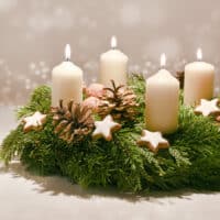 decorated wreath to celebrate advent with white burning candles, warm background with festive bokeh and white space.