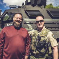 Chris Green, the founder of The Navigators First Response Ministry, standing in front of an armed vehicle with another police officer.