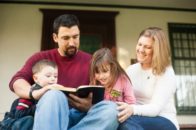 Father, mother and young daughter and son reading the Bible together during their daily devotional time