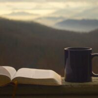 Daily devotional time with open Bible and coffee mug sitting on wood railing with mountain view