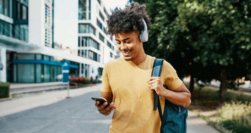 Young Mixed race millennial man listening to a podcast while wearing headphones, walking down a city street.