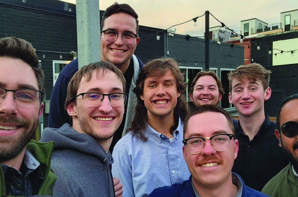A group of male college students take a group selfie while outside at a restaurant patio.