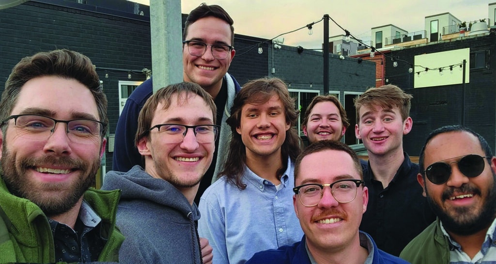 A group of male college students take a group selfie while outside at a restaurant patio.