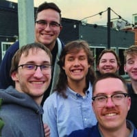 A group of male college students take a group selfie while outside at a restaurant patio.