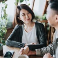 Happy young Asian couple having a coffee date in cafe, holding hands on coffee table. Drinking coffee and chatting. Enjoying a relaxing moment together.