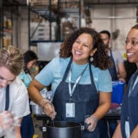 A diverse group of women smile and talk as they prepare food to serve at the soup kitchen.