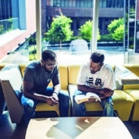 Two African-American men reading the bible together in an office lobby by a window.