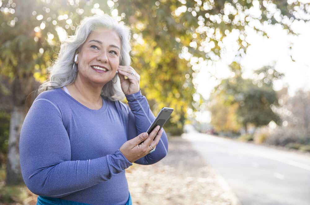 A woman wearing a purple shirt walking along a street listening to a podcast.