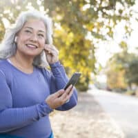 A woman wearing a purple shirt walking along a street listening to a podcast.