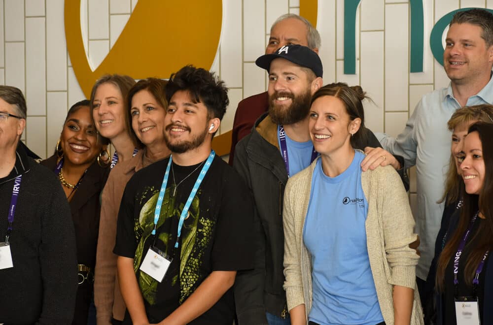 A group of Navigators staff stands together in front of The Navigators' logo.