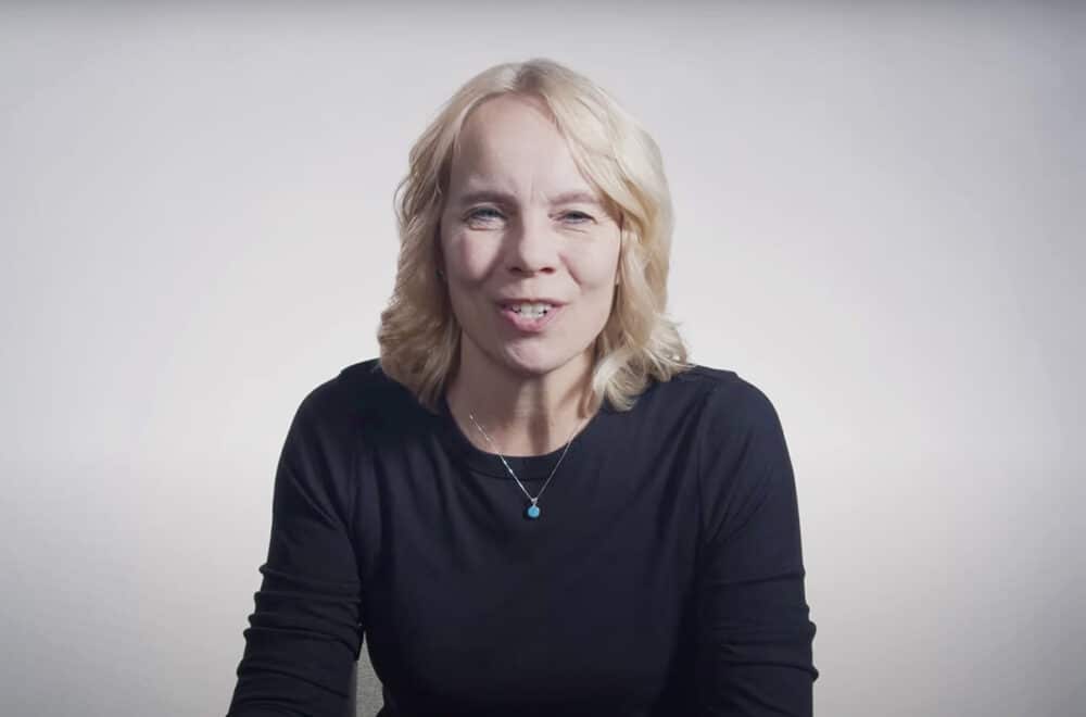 Vicki Gatchell speaking while sitting at a table with a white background.