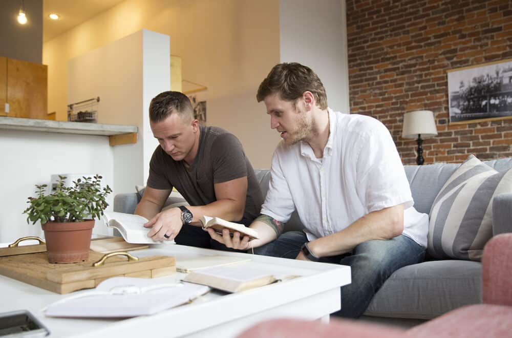 Two men sitting on a couch reading the Bible together.