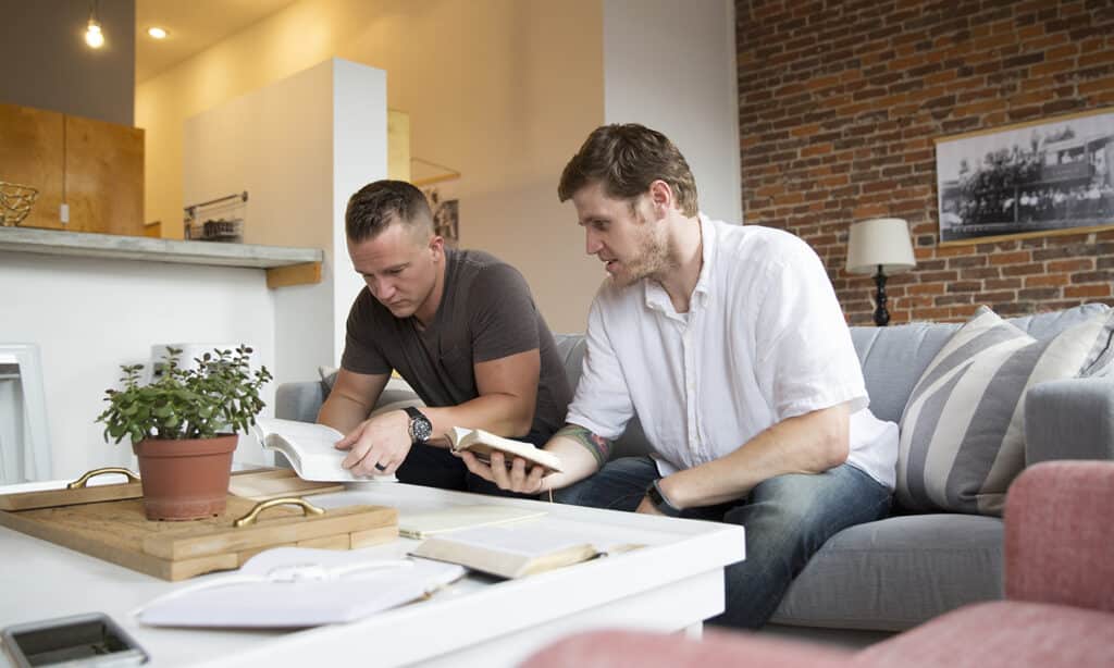 Two men sitting on a couch reading the Bible together.